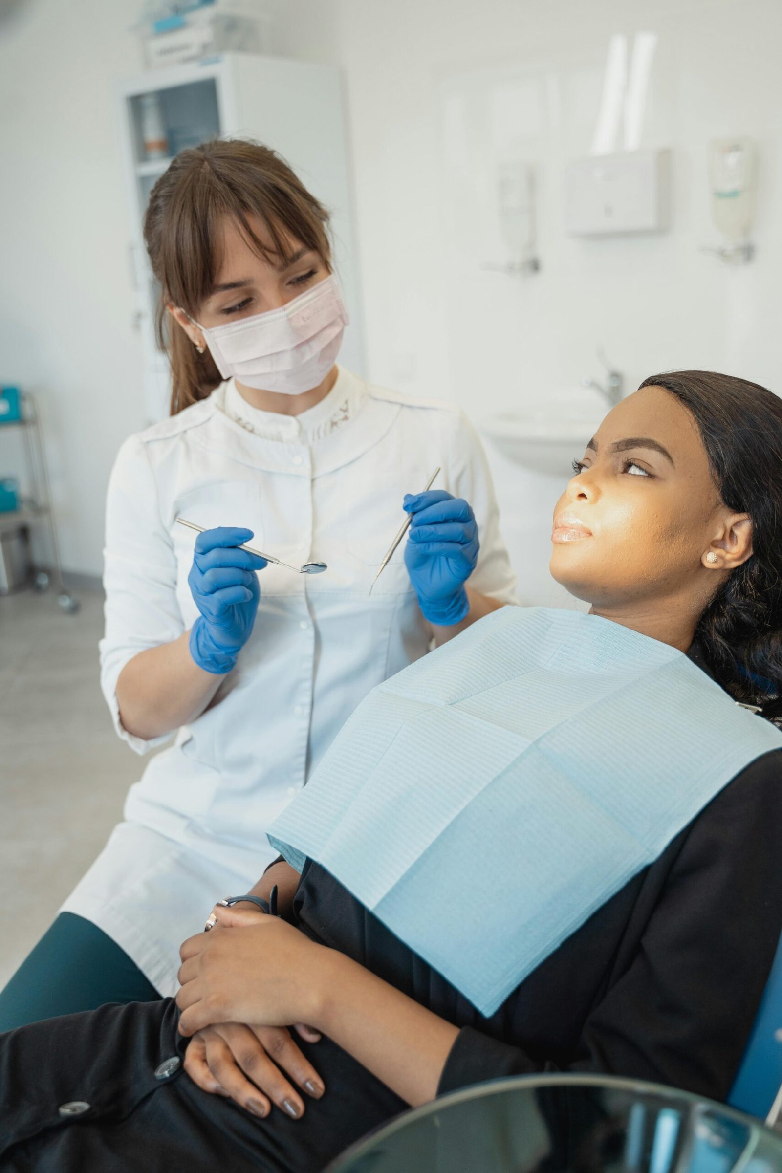 Dentist wearing gloves and facemask examines female patient in a dental clinic.